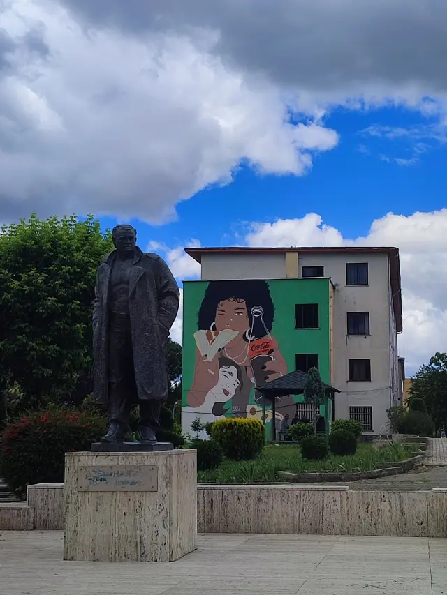 A bronze statue in front of a mural-painted building in Tirana