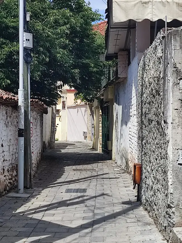 A narrow sunlit alley between stone walls in Tirana